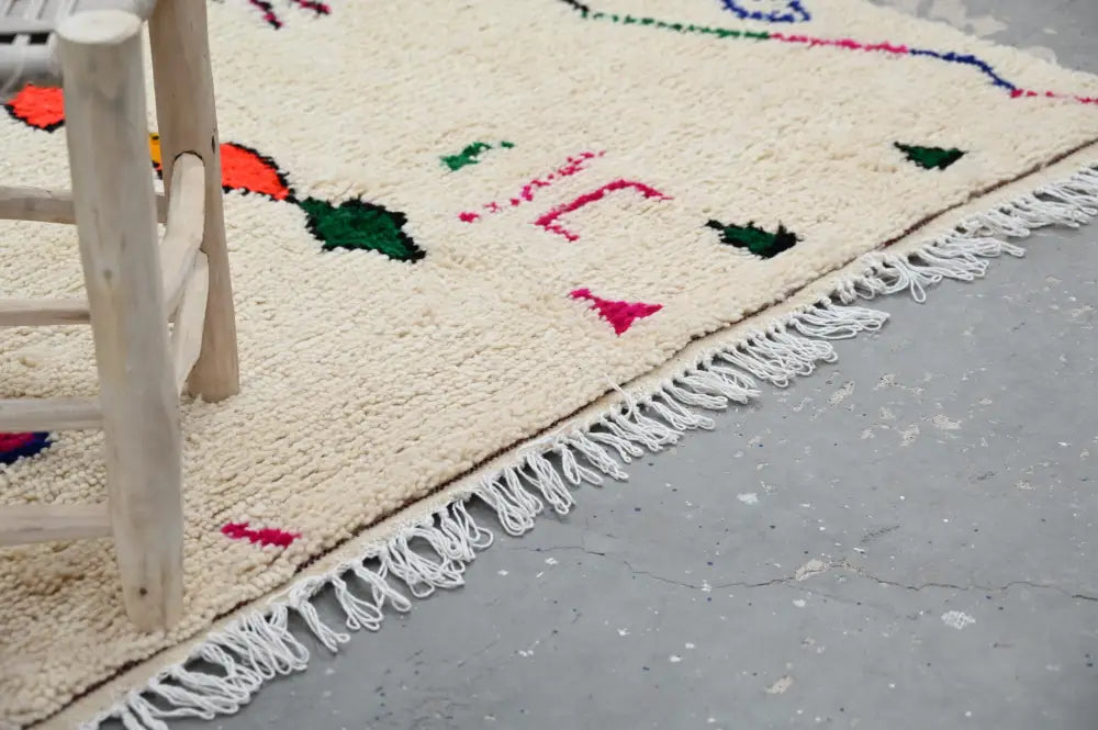 Cream-colored decorbites moroccan handmade traditional azilal rug with colorful geometric patterns and white fringe edges