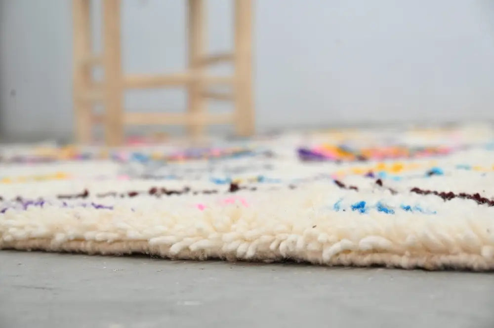A cream-colored moroccan handmade traditional azilal rug with vibrant geometric patterns and thick textured fringe