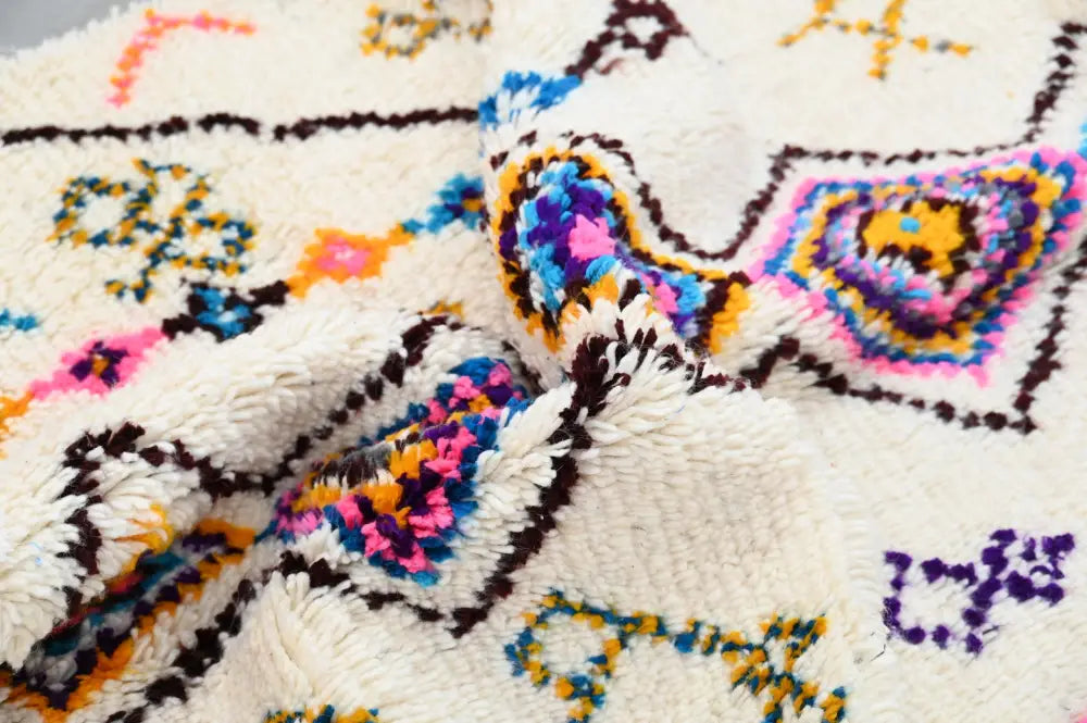 A plush off-white moroccan handmade traditional azilal rug with vibrant pink blue yellow and purple geometric patterns