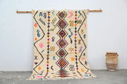 A vibrant cream-colored decorbites™ moroccan handmade traditional azilal rug with geometric patterns in bold hues