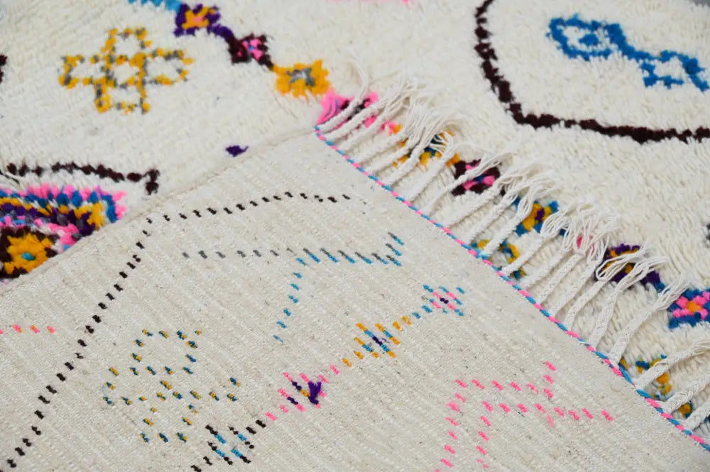 A moroccan handmade traditional azilal rug with a cream base, vibrant geometric patterns, and long white fringe