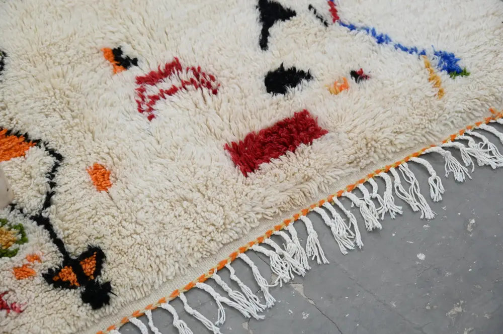 Cream-colored plush moroccan handmade traditional azilal rug with bold red black orange geometric patterns and white fringe