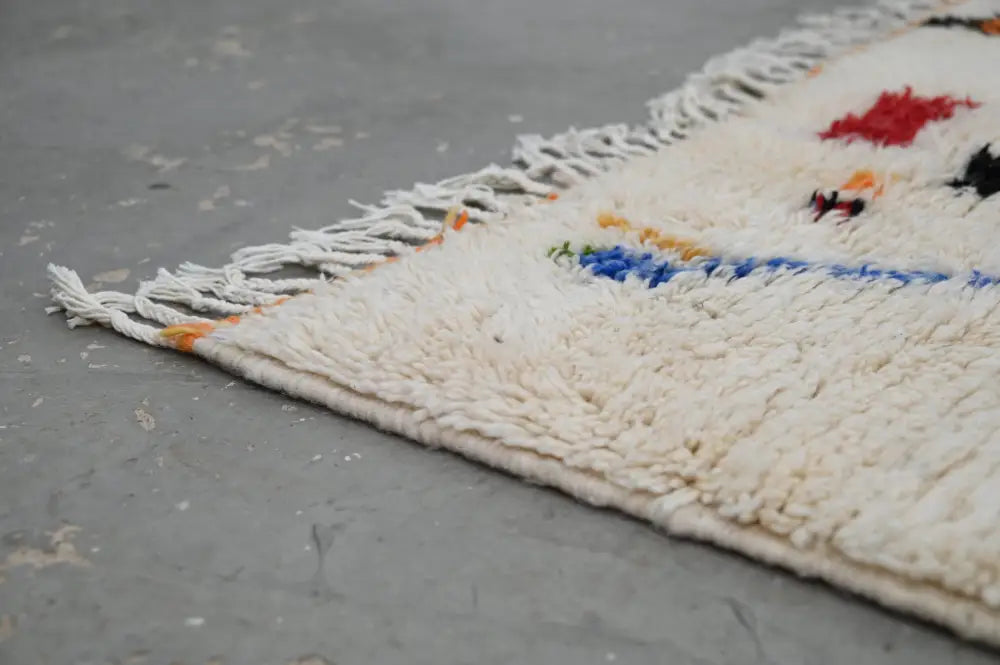 Cream-colored fluffy wool moroccan handmade traditional azilal rug with red blue black geometric patterns and white fringe