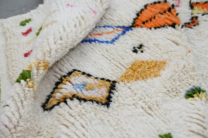 A plush off-white moroccan handmade traditional azilal rug with textured shaggy surface and vibrant geometric patterns
