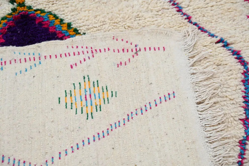 Cream-colored moroccan handmade traditional azilal rug with vibrant pink blue yellow and green geometric threadwork by decorbites