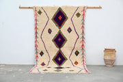 Beige moroccan handmade traditional azilal rug with bold purple diamond patterns and colorful geometric accents by DecorBites
