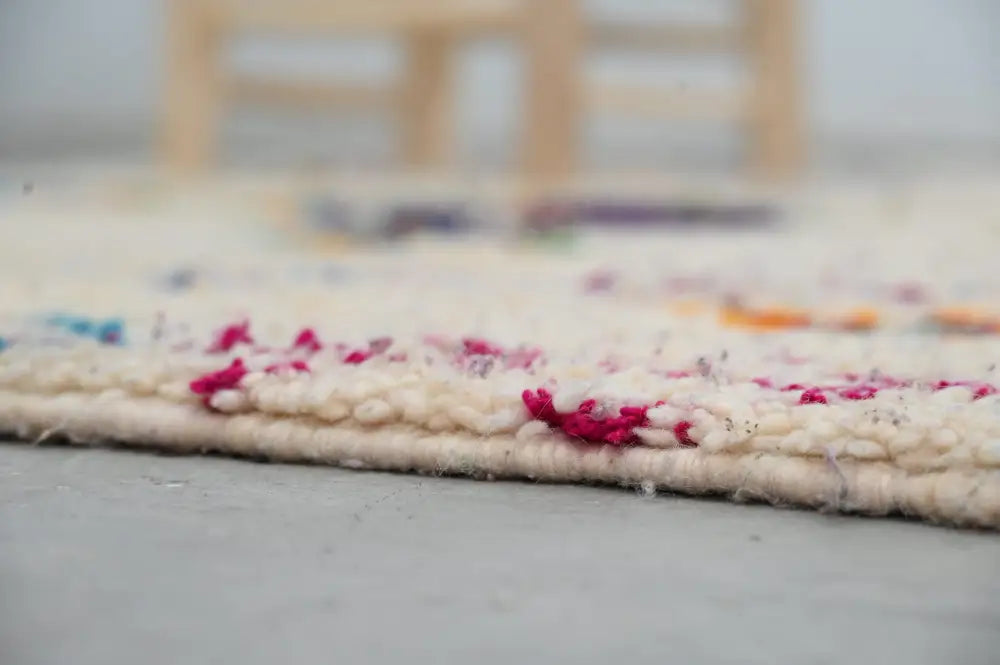 Cream-colored moroccan handmade traditional azilal rug with vibrant pink and multicolored accents along the edge