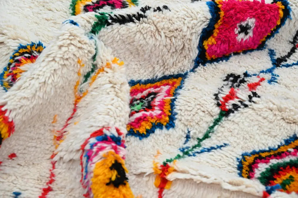 A cream-colored plush moroccan handmade traditional azilal rug with vibrant pink yellow green and blue geometric patterns