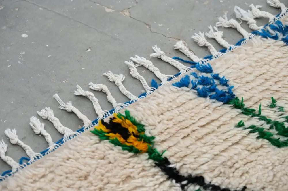 Cream-colored moroccan handmade traditional azilal rug with bold blue green geometric patterns and yellow flower motif