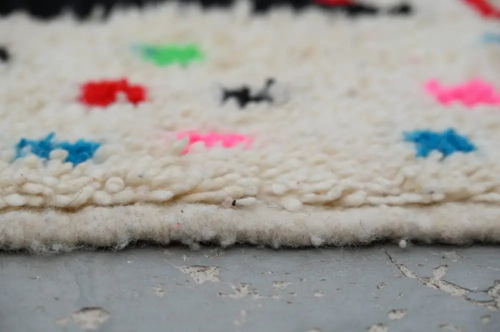 A cream-colored moroccan handmade traditional azilal rug with vibrant geometric patterns in red, blue, pink, and black