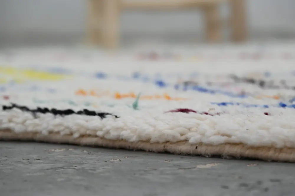 A soft white textured moroccan handmade traditional azilal rug with colorful geometric patterns in black blue yellow and red