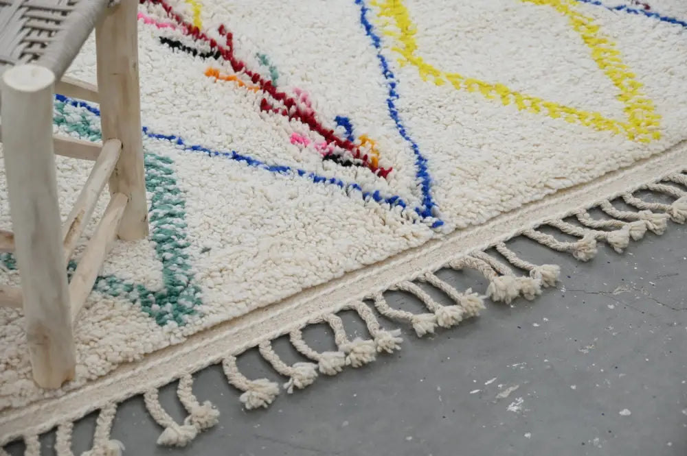 Cream-colored moroccan handmade traditional azilal rug with vibrant geometric patterns and fringed edge by decorbites