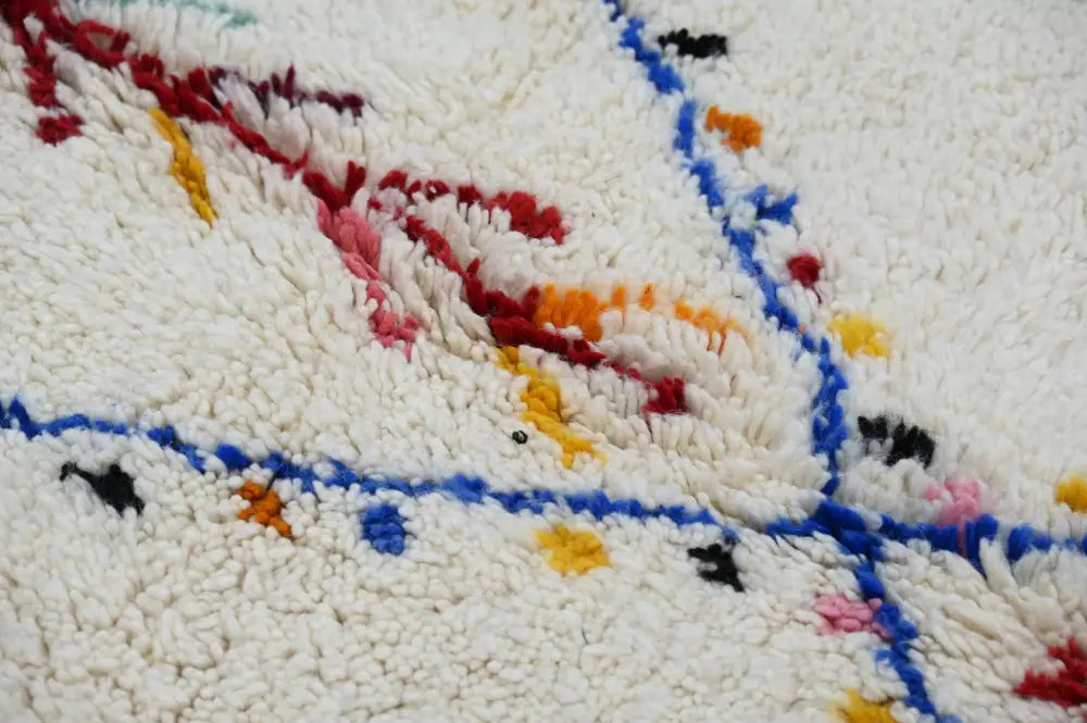 A plush white moroccan handmade traditional azilal rug with vibrant red blue yellow and black geometric patterns woven in fluffy texture