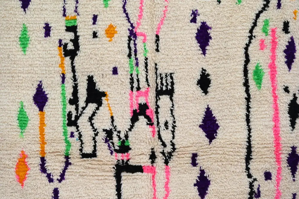 A cream-colored moroccan handmade traditional azilal rug with vibrant geometric patterns in purple green pink orange and black