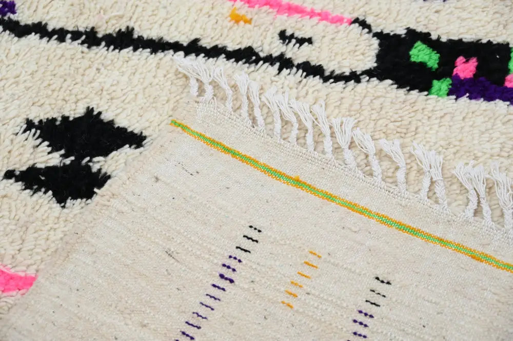 Cream-colored DecorBites™ Moroccan handmade traditional Azilal rug with bold black pink green purple patterns and white fringe