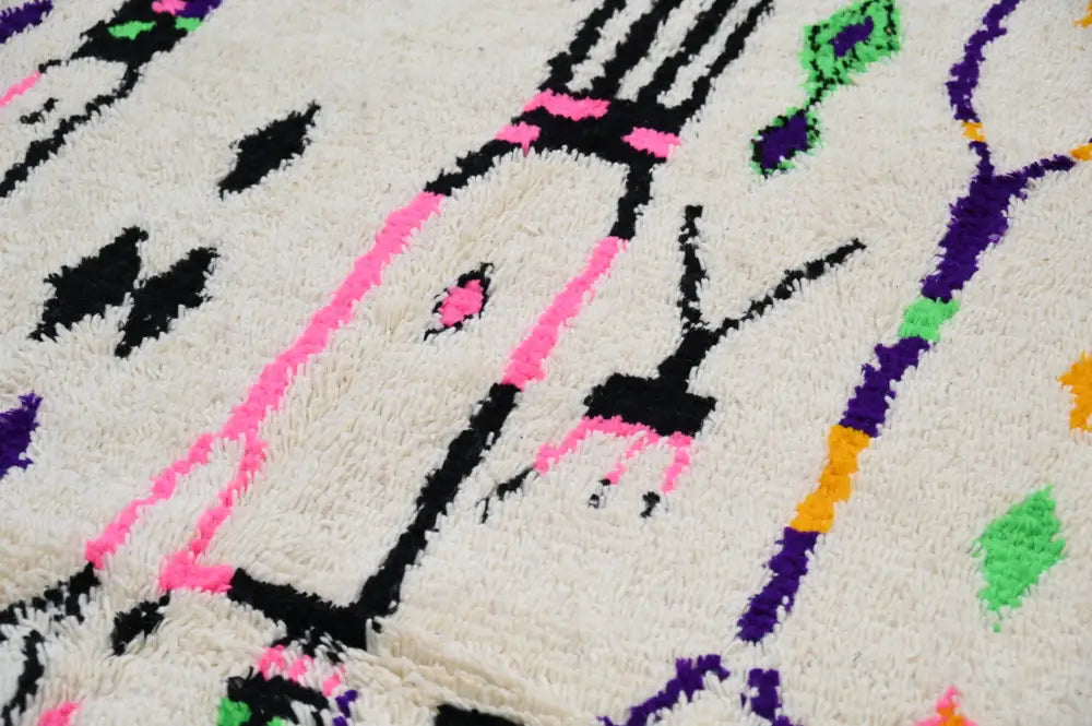 A plush off-white moroccan handmade traditional azilal rug with bold black pink purple green and yellow geometric patterns