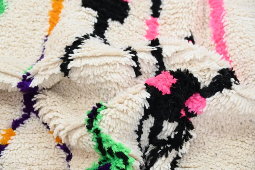 A cream-colored moroccan handmade traditional azilal rug with bold black pink green and orange geometric patterns by DecorBites