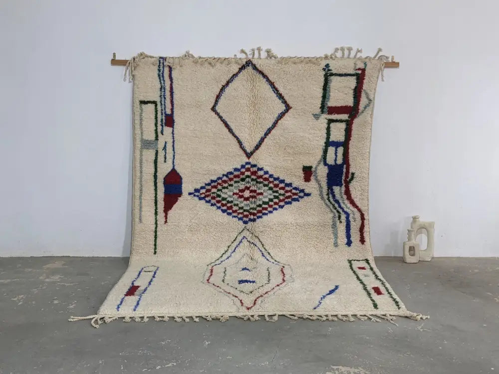 Cream-colored moroccan handmade traditional azilal rug with blue red green and black geometric patterns on woolen surface