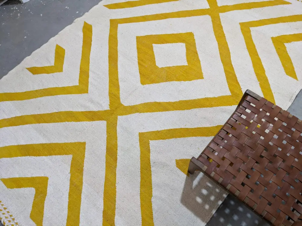 A cream-colored moroccan handmade traditional azilal rug with bold mustard-yellow geometric patterns by decorbites