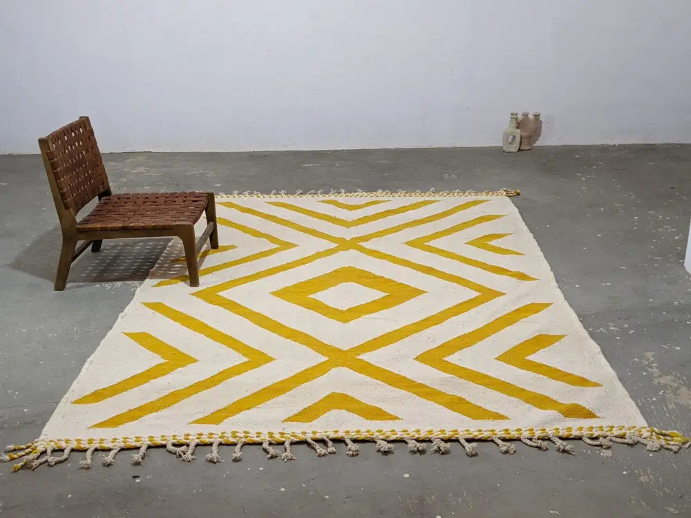 A cream-colored moroccan handmade traditional azilal rug with bold mustard-yellow geometric patterns and fringed edges