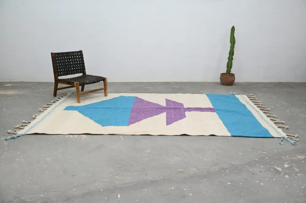 A cream-colored moroccan handmade traditional azilal rug with bold blue and purple geometric patterns and fringed edges
