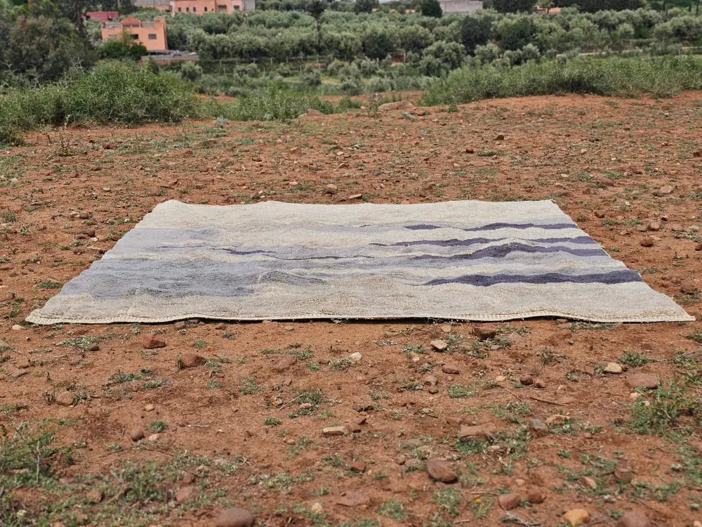 Decorbites™ moroccan handmade beni mrirt rug with textured beige base and faded blue-gray stripes on dry earth