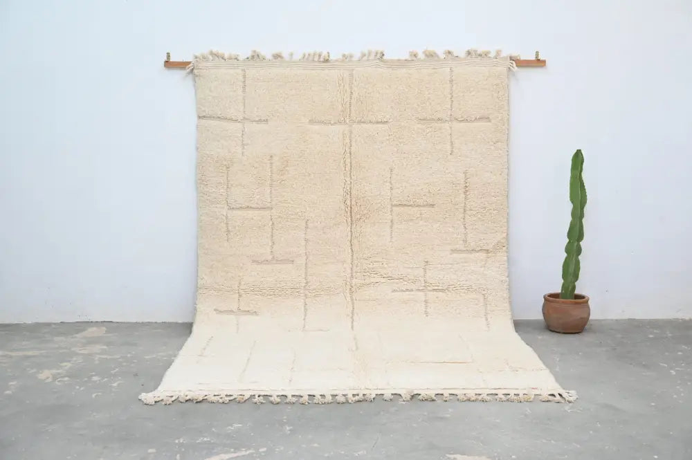Beige moroccan handmade beni ouarain carpet with geometric pattern and fringed edges hanging on wooden rods