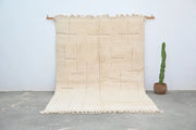 Beige moroccan handmade beni ouarain carpet with geometric pattern and fringed edges hanging on wooden rods