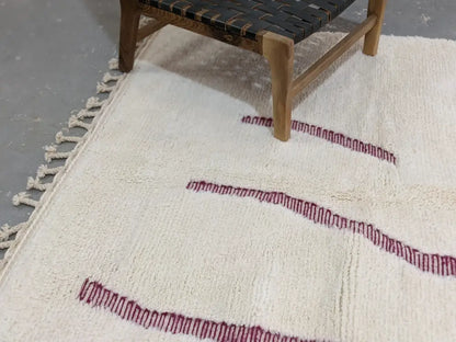 Cream-colored beni ouarain rug with textured wool surface and bold red stitched geometric edges moroccan handmade decorbites