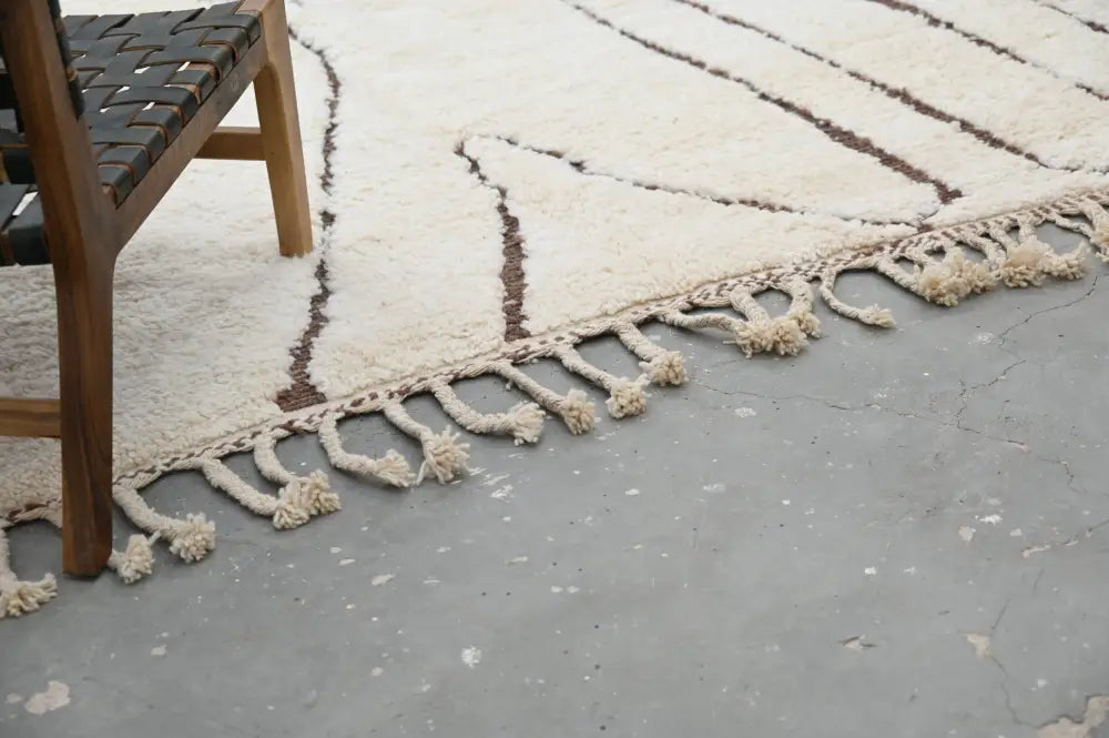 Cream-colored wool beni ouarain rug with dark brown geometric stripes and hand-knotted tassel fringe by DecorBites