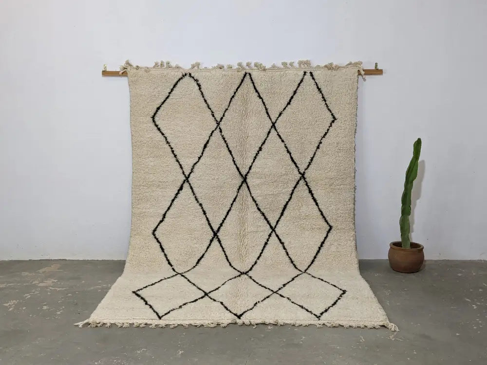 Cream-colored beni ouarain rug with black geometric diamond patterns and fringed edges moroccan handmade traditional design