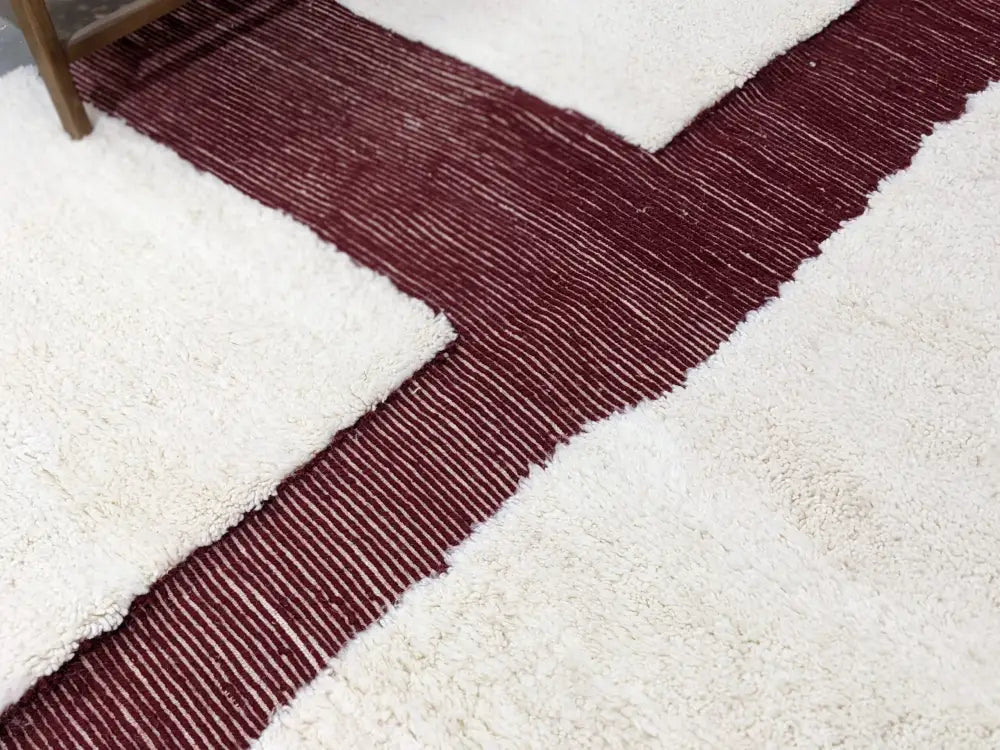 A cream-colored moroccan handmade beni ouarain rug with a central maroon striped band and fine white vertical lines