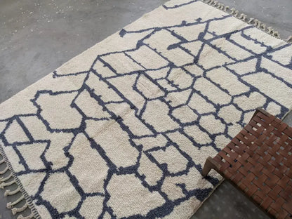 Cream-colored beni ouarain rug with bold navy geometric pattern fringed edges and textured weave moroccan handmade