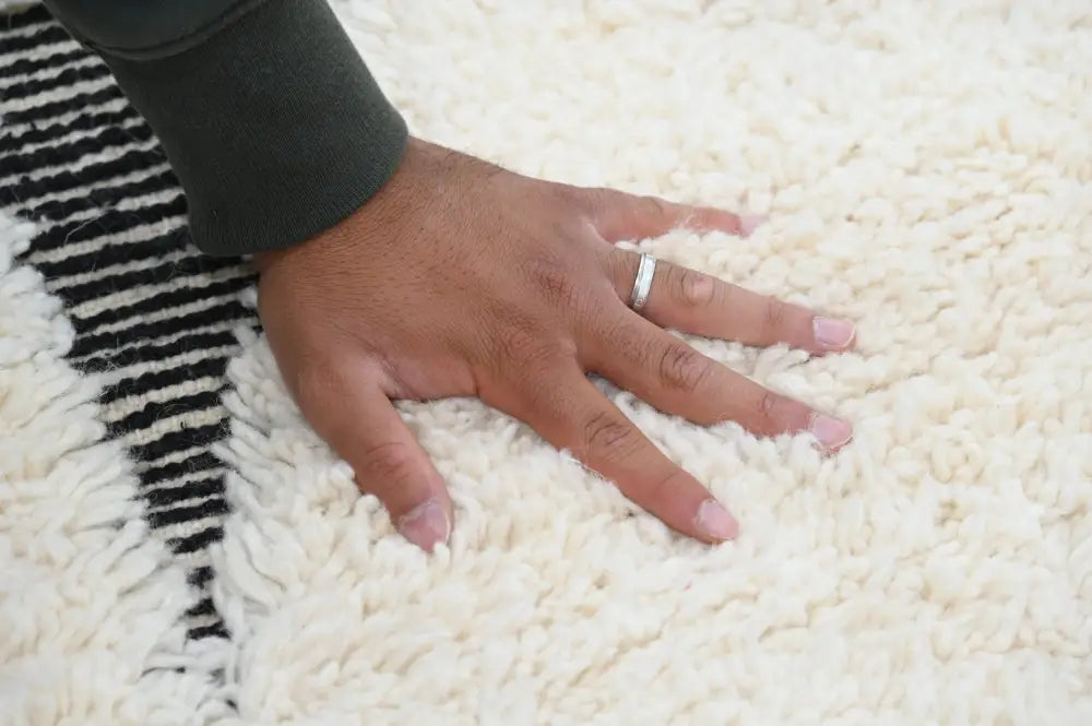 A cream-colored plush beni ouarain rug with a bold black and white striped border moroccan handmade design