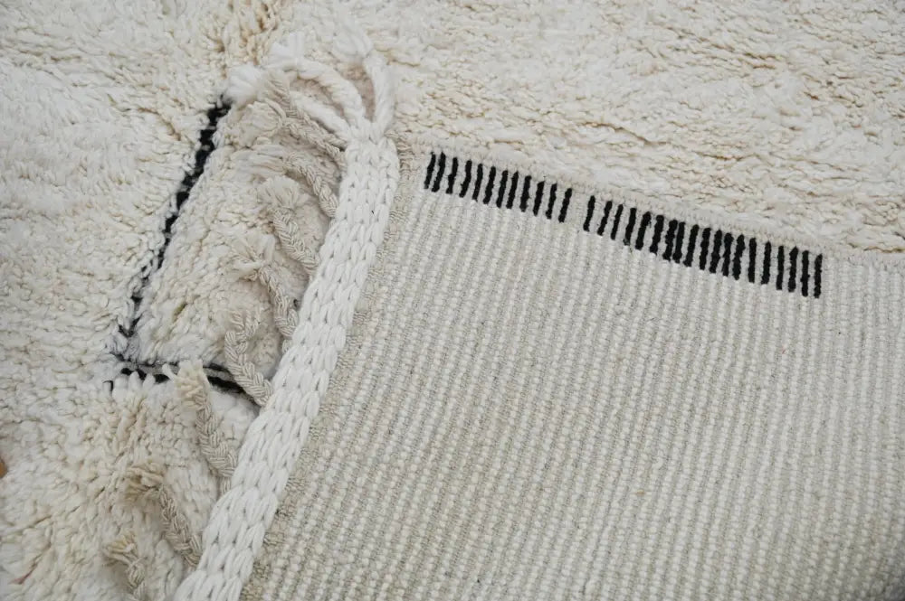 Cream-colored moroccan handmade beni ouarain rug with textured fluffy surface and black vertical stripes near edge