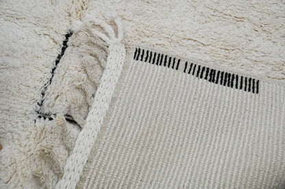 Cream-colored moroccan handmade beni ouarain rug with textured fluffy surface and black vertical stripes near edge