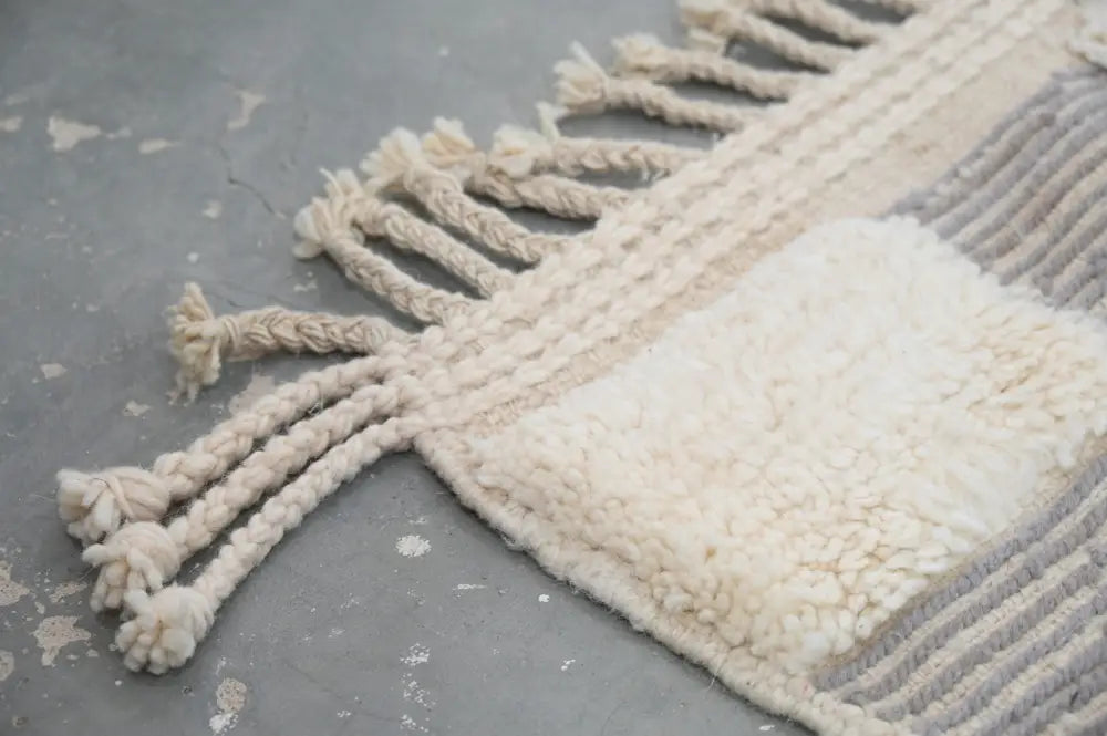 Cream-colored textured wool beni ouarain rug with braided fringe and gray woven accent stripes 300 x 203 cm