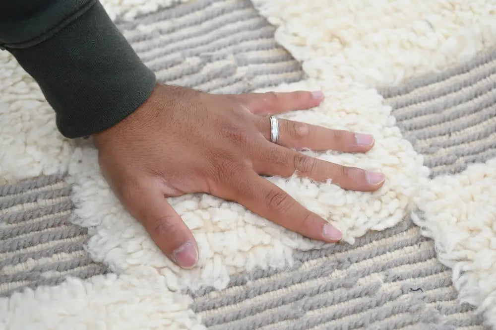 A hand rests on a cream and gray textured beni ouarain rug with plush looped pile in an interlocking design