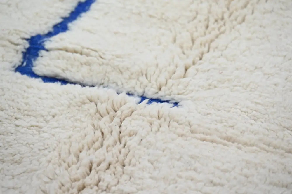 Cream-colored plush moroccan handmade beni ouarain rug with a bold blue stitched border 300 x 207 cm