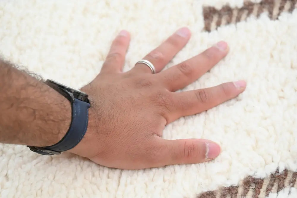 A hand with a dark blue silicone watch band rests on a cream beni ouarain rug with brown geometric patterns