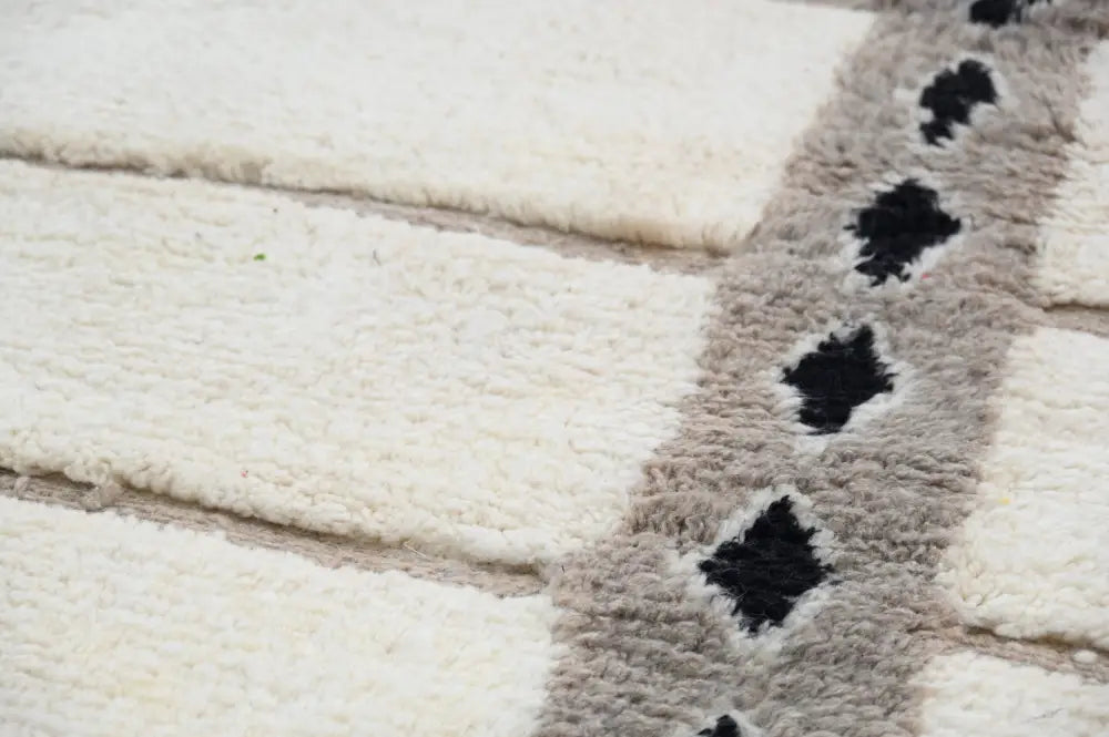 Cream-colored plush beni ouarain rug with textured surface and central gray stripe featuring black diamond patterns