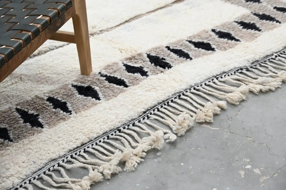 A cream-colored beni ouarain rug with black diamond geometric pattern on beige stripe and long fringe tassels moroccan handmade