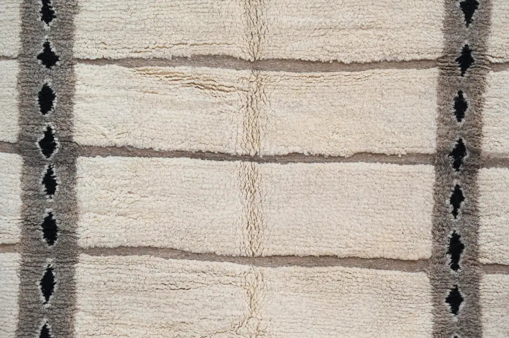 Cream-colored moroccan handmade beni ouarain rug with plush wool, grid pattern, and black diamond border design