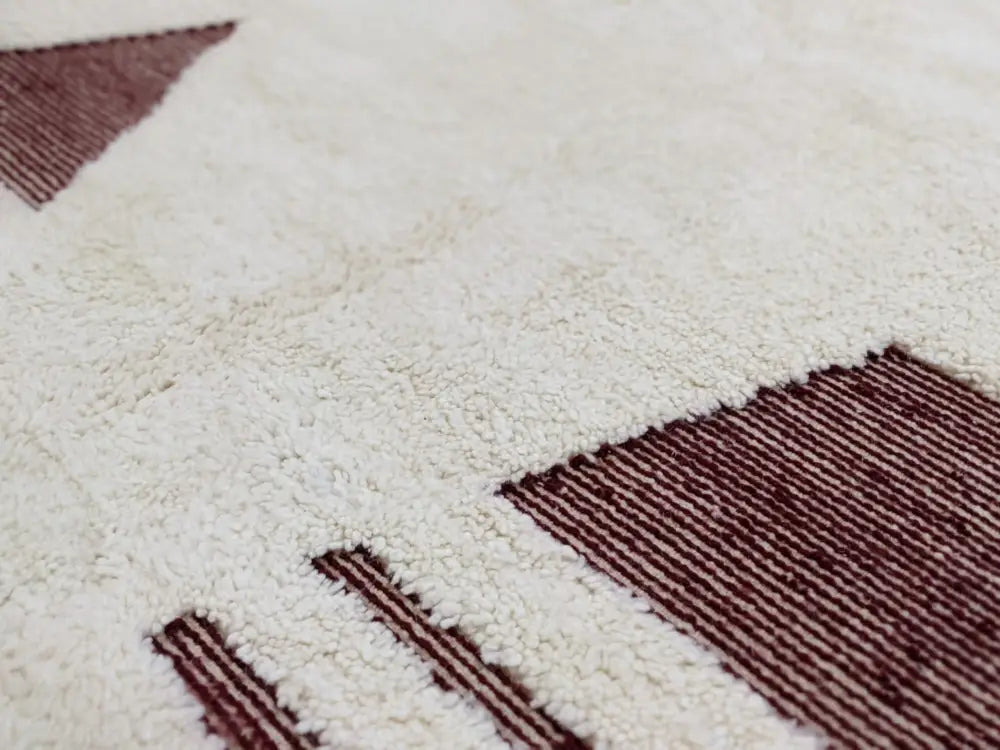 A plush white beni ouarain rug with geometric maroon patterns in a moroccan handmade textured high pile design