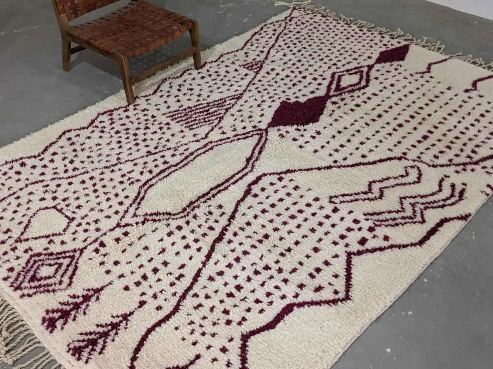 Cream-colored beni ouarain rug with deep burgundy geometric patterns and fringed edges by decorbites™