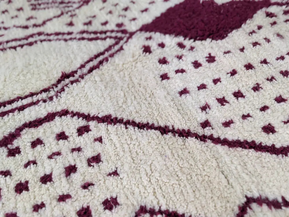 A cream-colored beni ouarain rug with intricate maroon geometric patterns woven into its textured surface