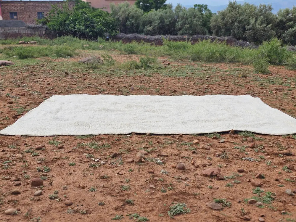 Off-white textured knit beni ouarain rug spread across dry earth showcasing moroccan handmade craftsmanship