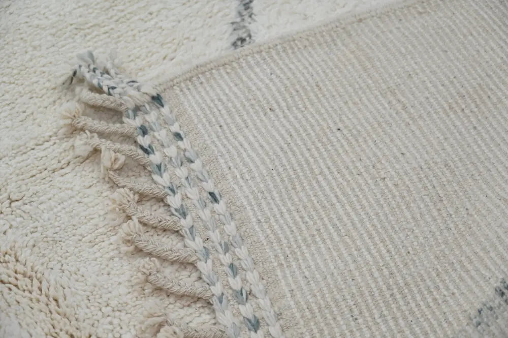 Cream-colored moroccan handmade beni ouarain rug with textured wool surface and fringed edges accented by gray threads