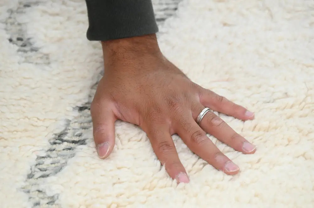 A hand with a silver ring rests on a cream-colored moroccan handmade beni ouarain rug with black geometric patterns