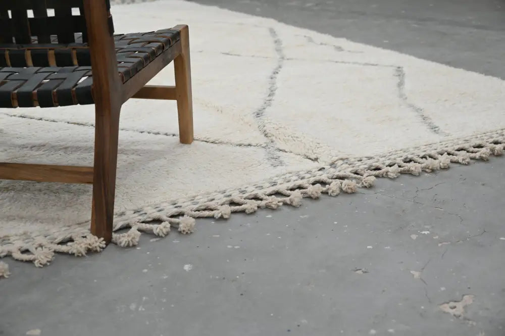 Cream-colored moroccan handmade beni ouarain wool rug with textured surface and dark gray geometric edge patterns